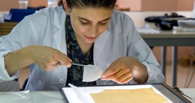 Paper conservator examining a fragile document with a soft brush